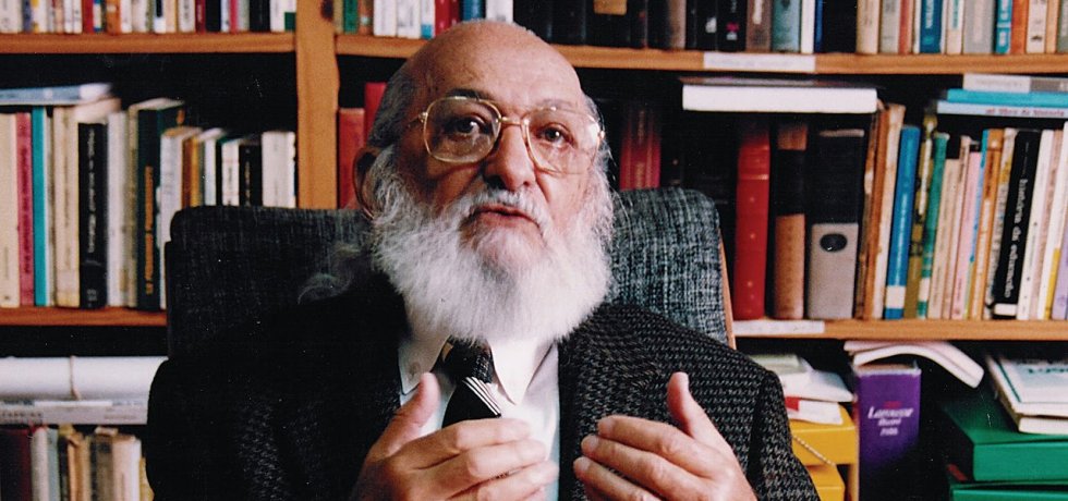 Paulo Freire com biblioteca ao fundo.